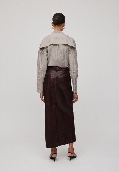 Camicia a righe con dettagli sulle spalle scese, abbinata a una gonna in pelle marrone scuro con cuciture e tasche, vista da dietro.