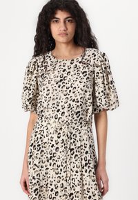 Leopardmønstret kjole i beige og sort, med pufærmer, en indsnævret talje med bånd og plisseret stof for tekstur og bevægelse.