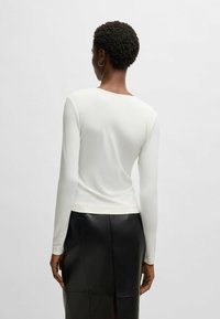 Top fitted a maniche lunghe in tessuto crema, con scollatura rotonda, texture liscia e design pulito, abbinato a una gonna in pelle nera.