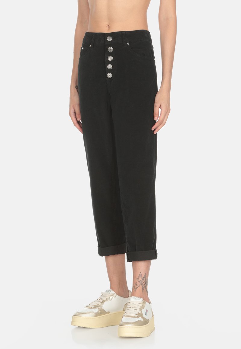 Pantaloni in corduroy neri con vita alta, chiusura a cinque bottoni argento e orli arrotolati. Abbinati a sneakers bianche e dorate.