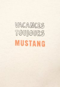 Krems krāsas kokvilnas T-krekls ar drukātu tekstu: "VACANCES TOUJOURS" pelēkā krāsā un "MUSTANG" oranžā krāsā. Gluda tekstūra ar brīvu piegriezumu.