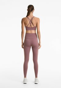 Muscle tanktop en legging set in gedempt mauve, met een crisscross rugdesign en hoge taille, gemaakt van rekbare stof.