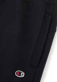 Pantalones de chándal negros de forro polar, con bolsillos laterales, cintura elástica y un pequeño logo bordado en blanco, rojo y negro.