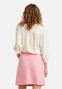 Witte blouse met pofmouwen, voorzien van subtiele gouden geborduurde stippen; gecombineerd met een gestructureerde roze minirok.