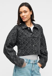 Κοντή τζιν ζακέτα σε σκούρο γκρι με γεωμετρικό σχέδιο, με κουμπιά στο κέντρο, μεγάλο γιακά και πλαϊνές τσέπες. Συνδυασμένη με ανοιχτόχρωμο μπλε τζιν παντελόνι.