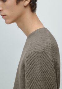 Brauner, strukturierter Pullover mit Rundhalsausschnitt und dezentem Waffelmuster, der eine eng anliegende Silhouette und weichen Stoff zeigt.