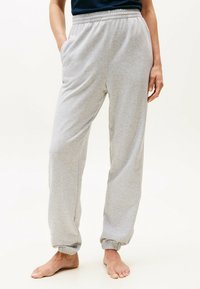 Grijze joggers van een katoenen mix met een elastische tailleband, zijzakken en elastische boorden, gepresenteerd op een model met blote voeten.