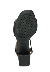 Sandalia de cuero negro con suela de goma texturizada que presenta perforaciones, tacón sólido y detalle de correa ajustable en el tobillo.