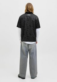 Chemise noire à manches courtes avec un motif texturé, design à col, et logo de l'UFC au dos, superposée sur une chemise blanche à manches longues.