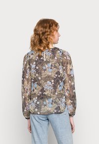 Blusa floral em tecido transparente com vários padrões de plantas em azul, verde e castanho; mangas bufantes e decote redondo nas costas.