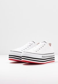 Vita canvas sneakers med en kraftig randig sula som har svarta och röda accenter. Rund tå, snörning, med metallöglor och stickade detaljer.