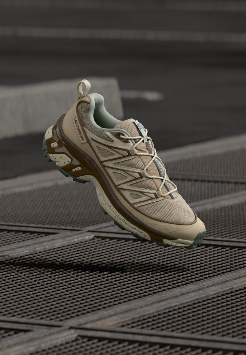 Beige sportig sko med ovandel i mesh och syntet, gröna detaljer, rundad tå, strukturerad sula och reflekterande inslag. Brun mellansula.