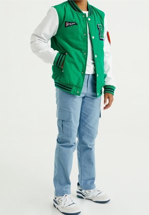 Vihreä yliopistotakki valkoisilla hihoilla, raidalliset hihansuut ja päällysteet. Yhdistettynä vaaleansiniin cargo-housuihin ja valkoisiin tennareihin, joissa on yksityiskohtia.