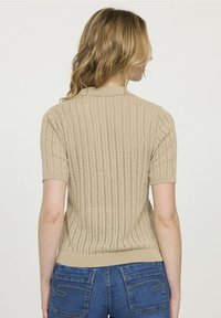 Pull en tricot beige avec un design texturé à côtes, des manches courtes et un ourlet ajusté. Présenté de dos, avec un col simple.