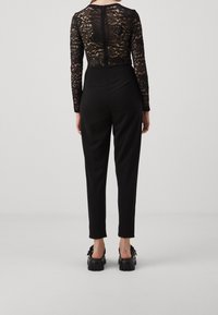 Svart jumpsuit med en figurnära design, en bodice i spets och långa ärmar, kompletterad med smala byxor och kraftiga skor.