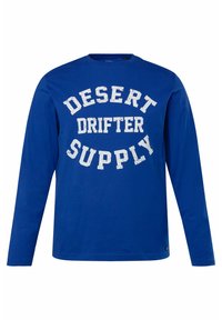 Maglietta a maniche lunghe in cotone blu con testo bianco sbiadito che recita "DESERT DRIFTER SUPPLY" sulla parte anteriore. Morbido al tatto e dal design casual.