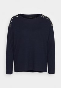 Granatowy sweter z długim rękawem o luźnym kroju, z perłowymi akcentami na ramionach i okrągłym dekoltem. Miękki materiał o delikatnej fakturze.