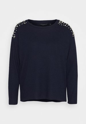 Laivastonsininen pitkähihainen neule, jossa on rento mitoitus. Olkapäillä helmikoristeet ja pyöreä pääntie. Pehmeä materiaali, jossa on hieman tekstuuria.