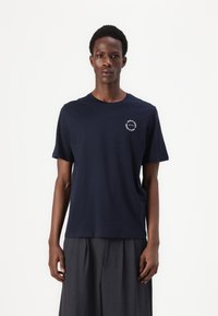 Navy blue cotton t-shirt with a round neckline, short sleeves, and a circular white logo on the left chest. Smooth texture and regular fit.