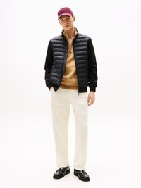Svart puffjakke over en beige sweatshirt, kremfargede bukser og svarte sko. Burgunder cap fullfører antrekket og fremhever en uformell stil.