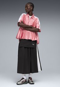 Roze satijnen top met rits en peplumzoom, gecombineerd met een zwarte gelaagde rok. Accenten in het wit en opvallende sneakers maken de outfit compleet.