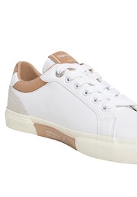 Hvit joggesko med brune lærdetaljer og semsket hæl. Har rundet tå, flate lisser og teksturert gummisåle. Merking på tunge og side.