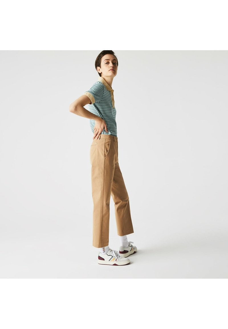 Polo bleu clair à carreaux avec des bordures beige, associé à un pantalon droit beige et des baskets avec des accents blancs, rouges et bordeaux.