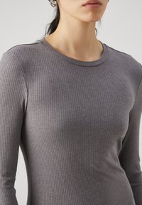 Γκρίζο ριγωτό μακρυμάνικο μπλουζάκι με στρογγυλή λαιμόκοψη, που διαθέτει εφαρμοστή σχεδίαση και μαλακή υφή. Η αόρατη ραφή ενισχύει την ομαλή εμφάνιση.