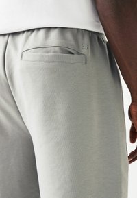 Shorts de sport gris clair avec taille élastique, dotés d'une poche arrière unique et d'une marque discrète près de la taille. Texture lisse.