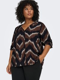 Brown and black patterned button-up shirt with a V-neck, featuring zigzag designs, relaxed fit, and rolled sleeves. Worn with black pants.
