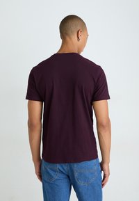Bordeaux kortærmet T-shirt med rund hals, tætsiddende design og glat tekstur. Båret med blå jeans, set bagfra.