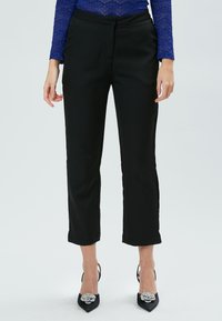 Zwarte cropped broek met een gladde textuur, met een getailleerde pasvorm en subtiele zijzakken. Geraadpleegd met zwarte hoge hakken en diamanten accenten.