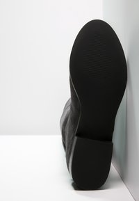 Black suede ankle boot with a rounded toe, textured black rubber sole, and a slightly elevated heel. The design features a smooth surface.