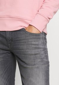 Světle růžová mikina s žebrovanými manžetami, spárována s úzkými tmavě šedými džíny s jemnou texturou a designem pěti kapes.