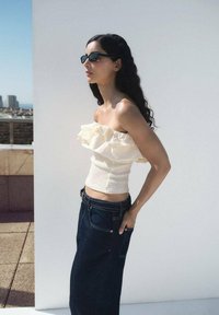 Top crema senza spalline con design arricciato, abbinato a jeans a vita alta blu scuro con cuciture in evidenza e tasche laterali.