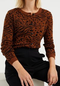 Brun och svart leopardmönstrad cardigan med långa ärmar, rund halsringning och sex svarta knappar fram. Mjuk, stickad tygtextur.