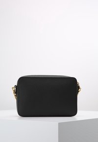 Černá koženková crossbody taška s obdélníkovým tvarem, texturovaným povrchem, zlatými kovovými detaily a zipovým uzávěrem.