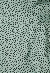 Světlá zelená látka s černým květinovým vzorem, se zavinovacím designem a pasem, s hladkou texturou a sklady.