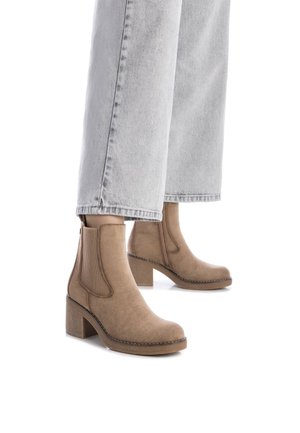 Botas de tobillo marrones de ante con paneles laterales elásticos, un tacón bloque y costuras decorativas a lo largo de la suela, combinadas con jeans de mezclilla claros.