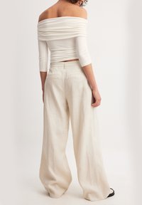 Witte off-the-shoulder top met geplooide textuur en driekwartmouwen, gecombineerd met losse, lichtbeige linnen wijde broek.