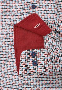Korte mouwen shirt van een gemêleerde stof in blauw, rood en zwart. Voorzien van een rode kraagvoering, blauwe knopen en een contrasterend knoopdesign.