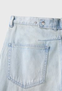 Tissu denim bleu clair montrant la poche arrière et la ceinture avec un bouton en métal sur un jean.