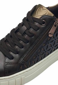 Sneaker in pelle nera con un intricato motivo a intaglio, dettagli in bronzo, lacci piatti, zip laterale e suola in gomma bianca per stabilità e aderenza.