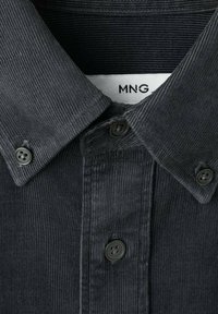 Camisa de pana negra con cuello tipo polo, que presenta dos botones, tela texturizada de canalé y una etiqueta blanca con la leyenda "MNG."