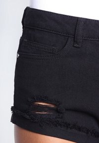 Pantalones cortos de mezclilla negra con un dobladillo deshilachado, estilo recortado, detalles en los bolsillos y una sección rasgada para un look desgastado.