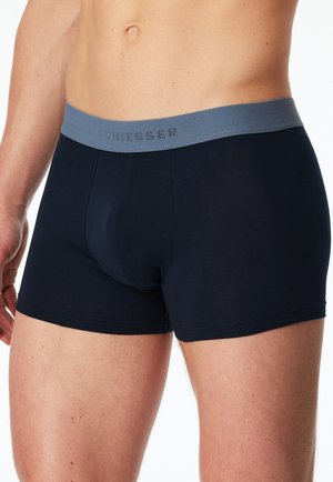 Torso masculino con bóxers azul oscuro con una cintura gris que lleva el nombre de la marca "SCHIESSER".