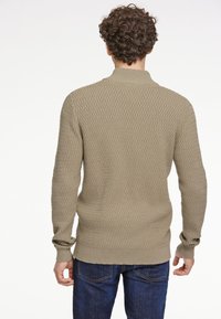 Jersey de punto en color beige claro con un patrón de diamantes texturizado, con cuello y puños de canalé, combinado con jeans azul oscuro.