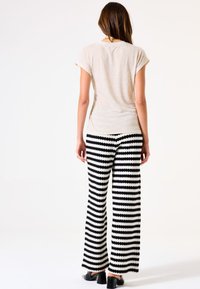 Helles beiges T-Shirt mit aufgeschlagenen Ärmeln, kombiniert mit schwarz-weiß gestreiften, weiten Hosen mit strukturiertem Strickdesign und Blockabsätzen.