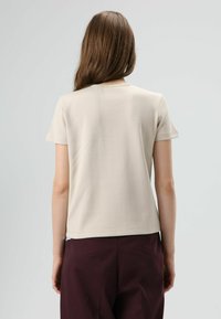 Beige short-sleeve t-shirt, made of soft cotton, with a simple crew neckline and a straight cut, paired with dark burgundy pants.
