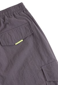 Grå tyg cargo-shorts med elastisk midja, sidofickor och en bakficka med en grön detaljerad etikett. Slät, lätt textur.